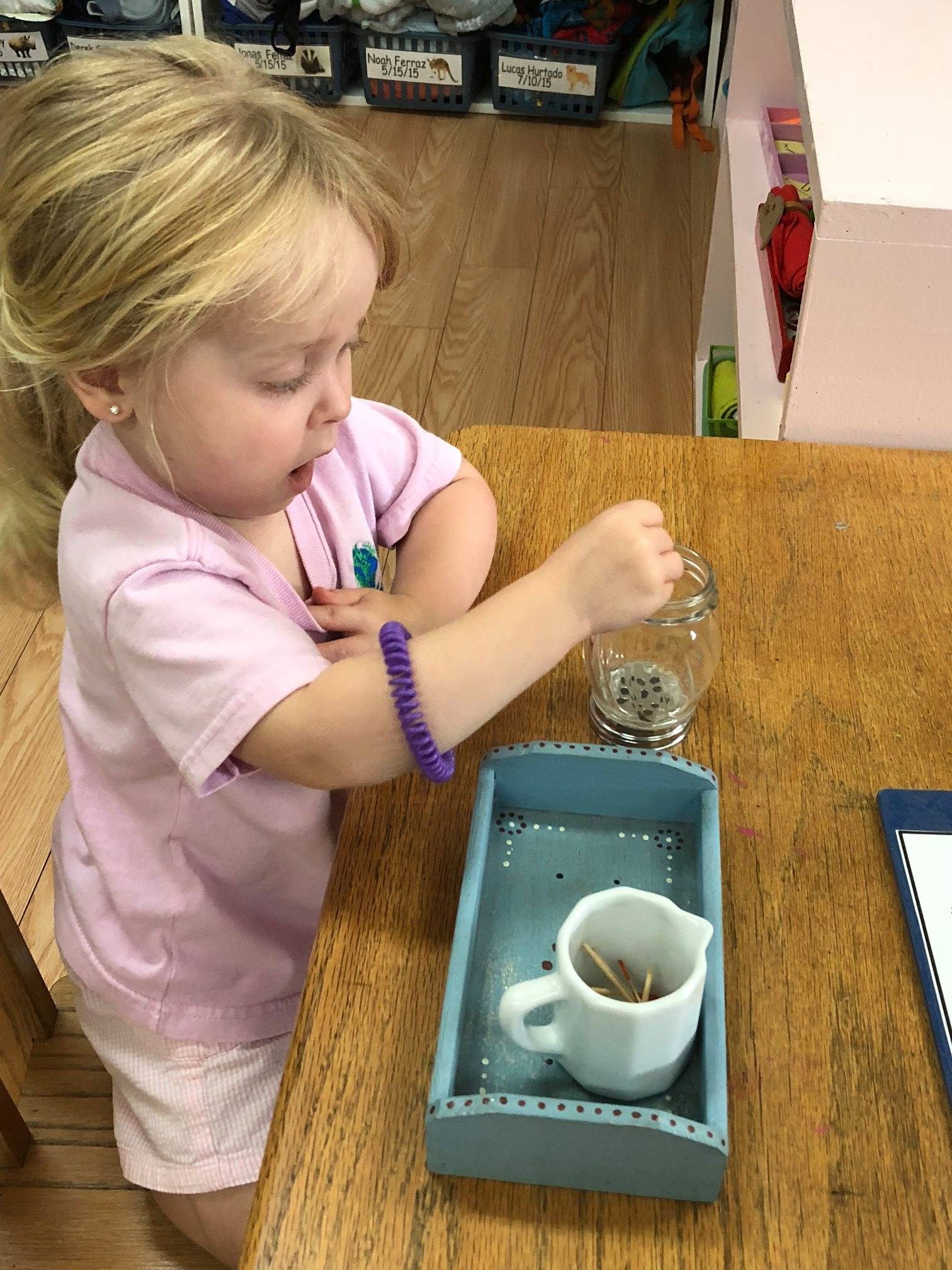Toddler girl practicing pouring water with a small pitcher